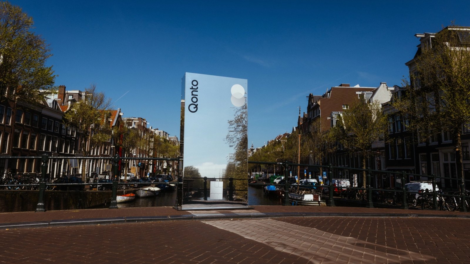 A mirror pillar on a canal bridge reflecting the Amsterdam canal houses and sky