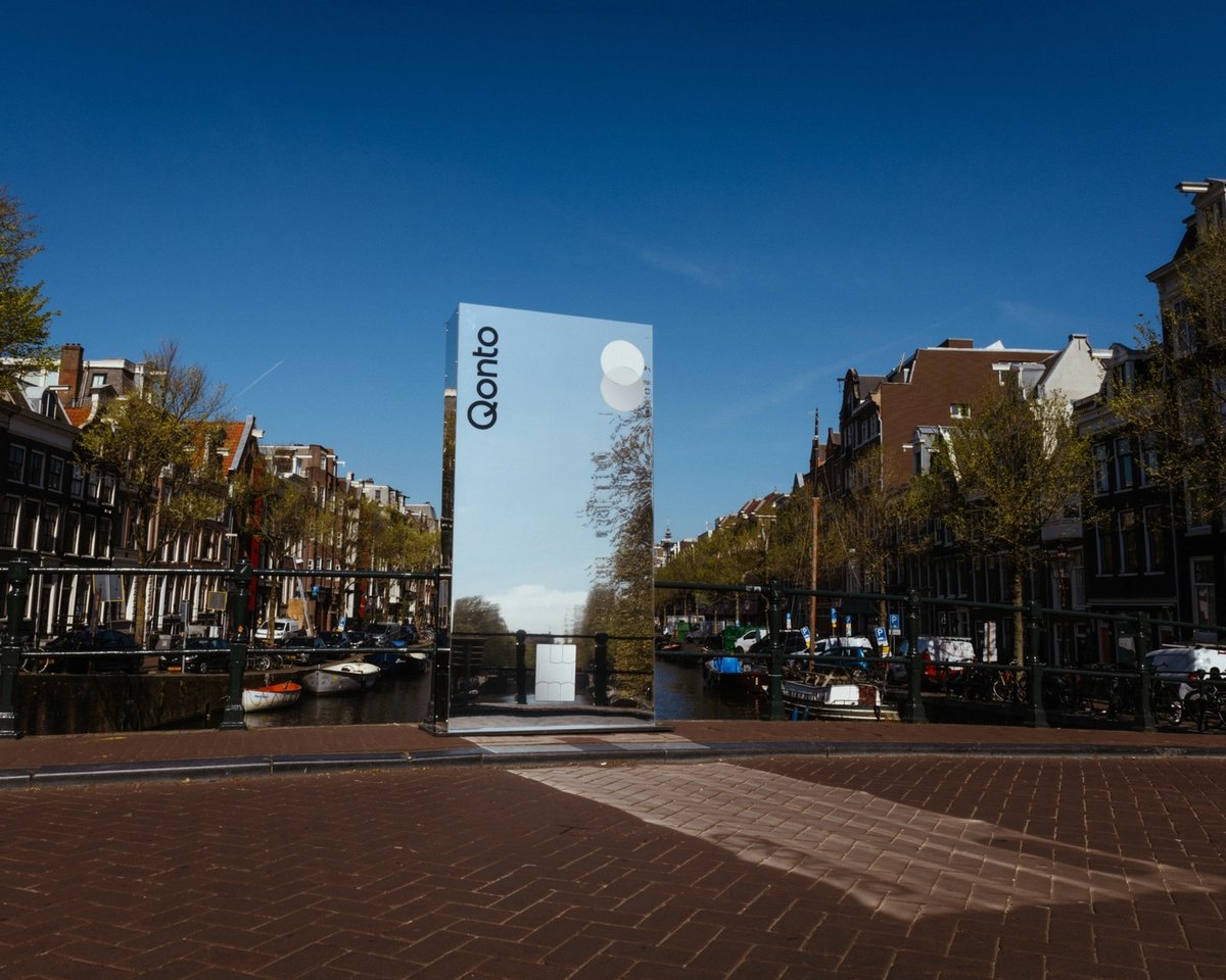 A mirror pillar on a canal bridge reflecting the Amsterdam canal houses and sky