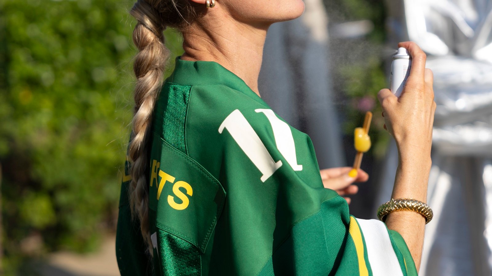 A guest in a green Dolly jersey spraying sunscreen, silver drape behind her
