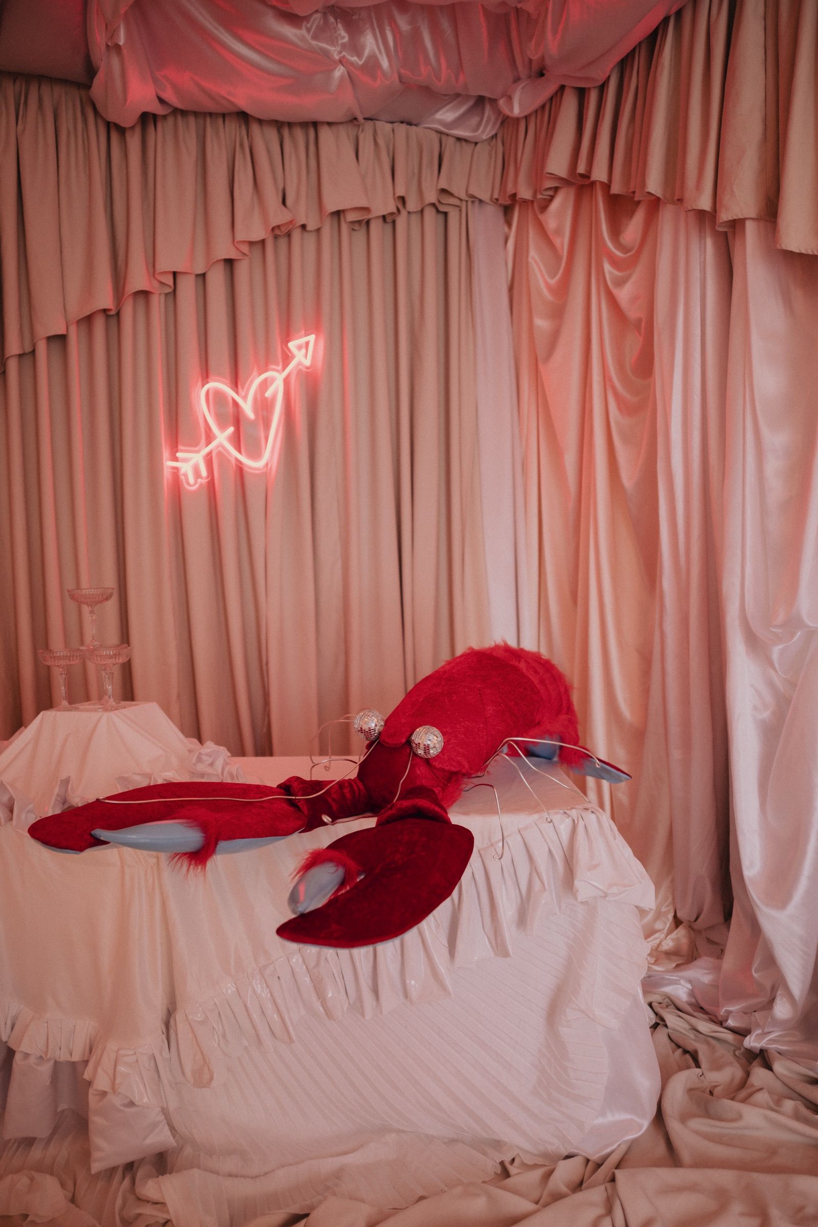 The red lobster on a white cloth under the neon heart, between pink and cream drapes