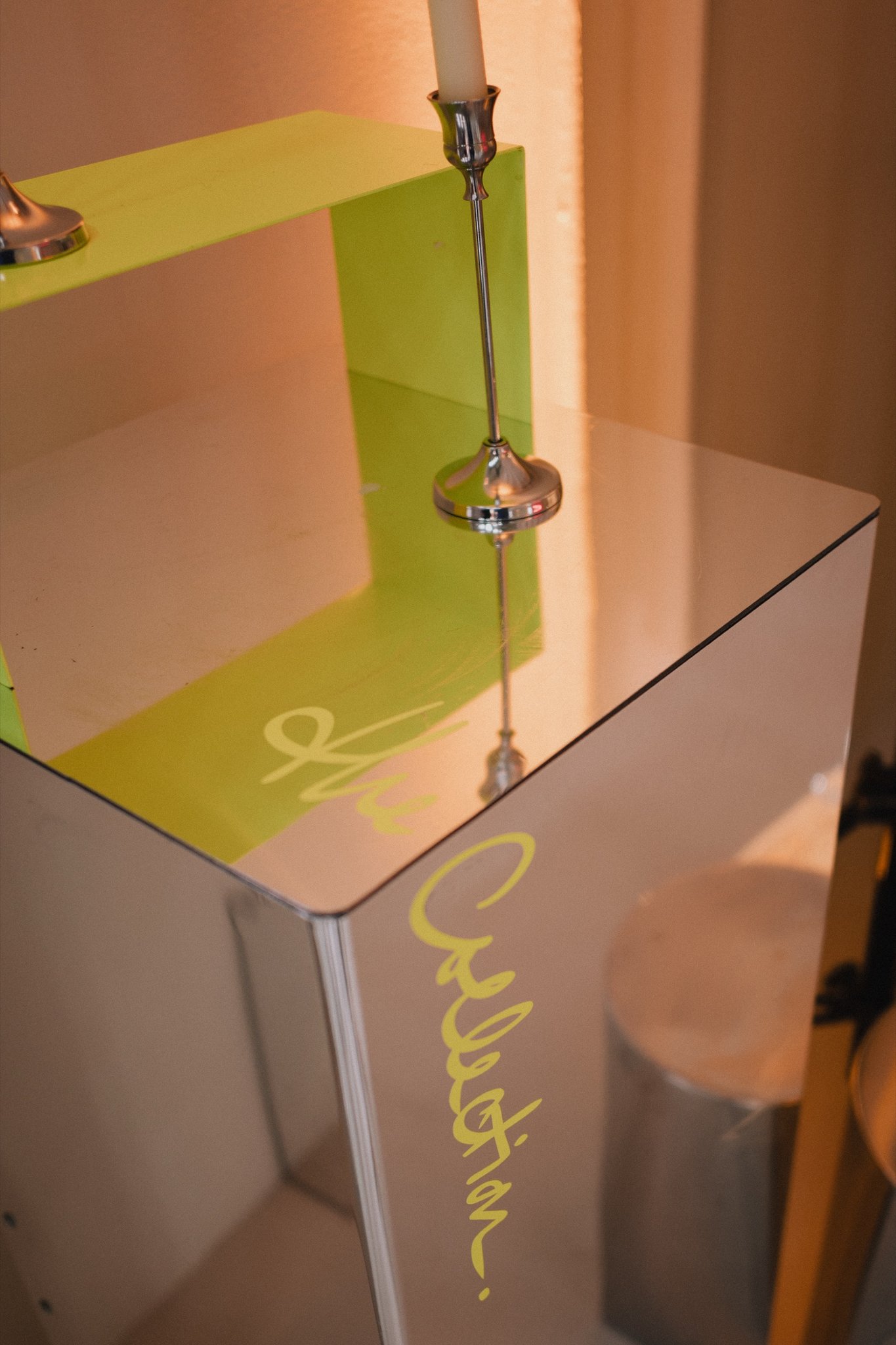 A mirror plinth with a lime-green candle holder and the handwritten The Collection wordmark