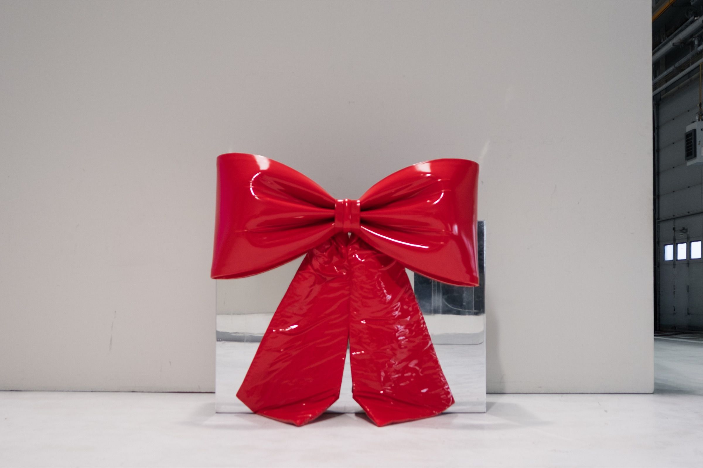 A red patent bow leaning against a mirror panel in an empty white hall