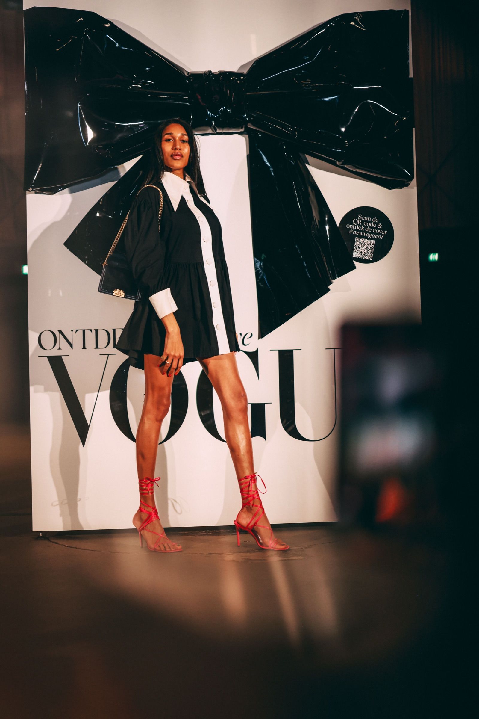 A model in black and white in front of the VOGUE box and its giant black bow