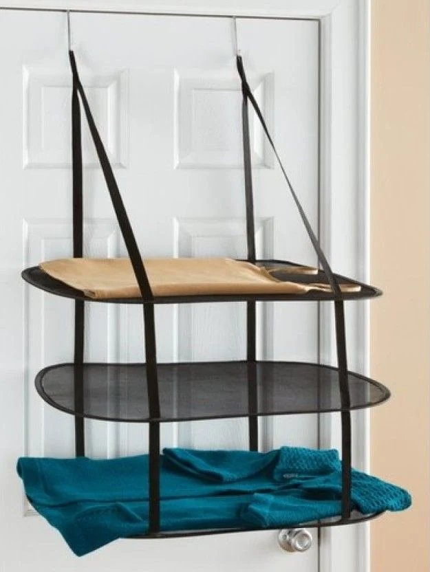 A three-tier black mesh drying rack holding clothes, hanging over a white door.