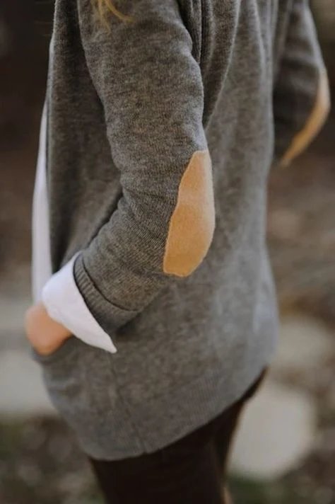 A person wearing a gray sweater with tan elbow patches and a white shirt cuff.