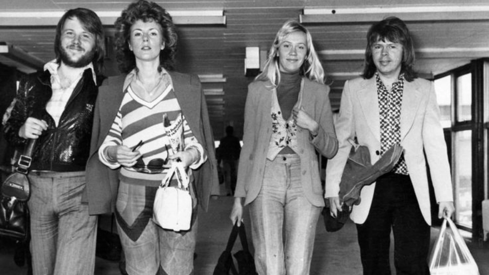 Black-and-white photo of the four members of ABBA walking through an airport terminal.
