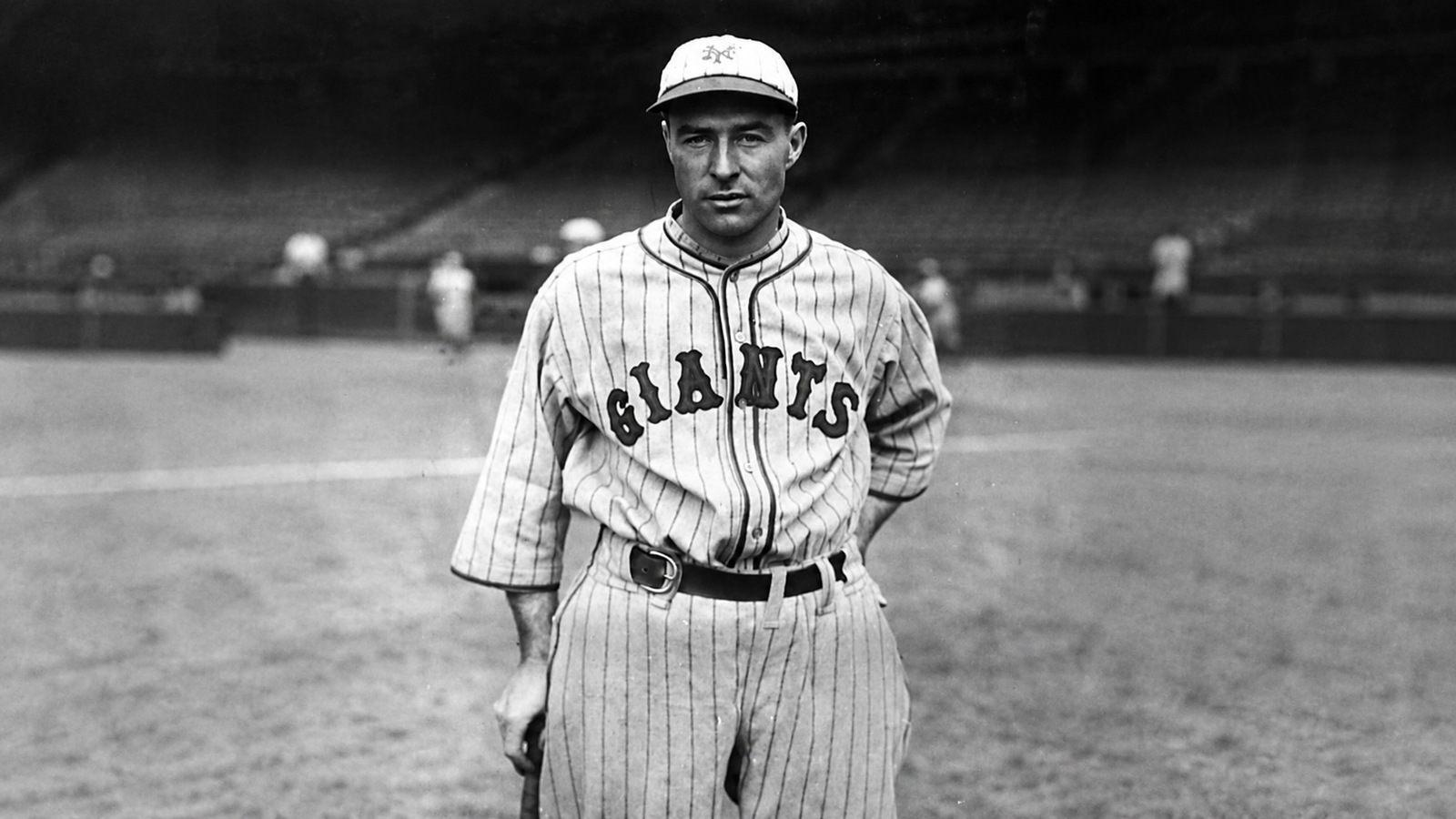 Schwarz-Weiß-Foto eines Baseballspielers in einem Nadelstreifen-Trikot mit der Aufschrift „GIANTS“, der auf einem Spielfeld einen Schläger in der Hand hält.