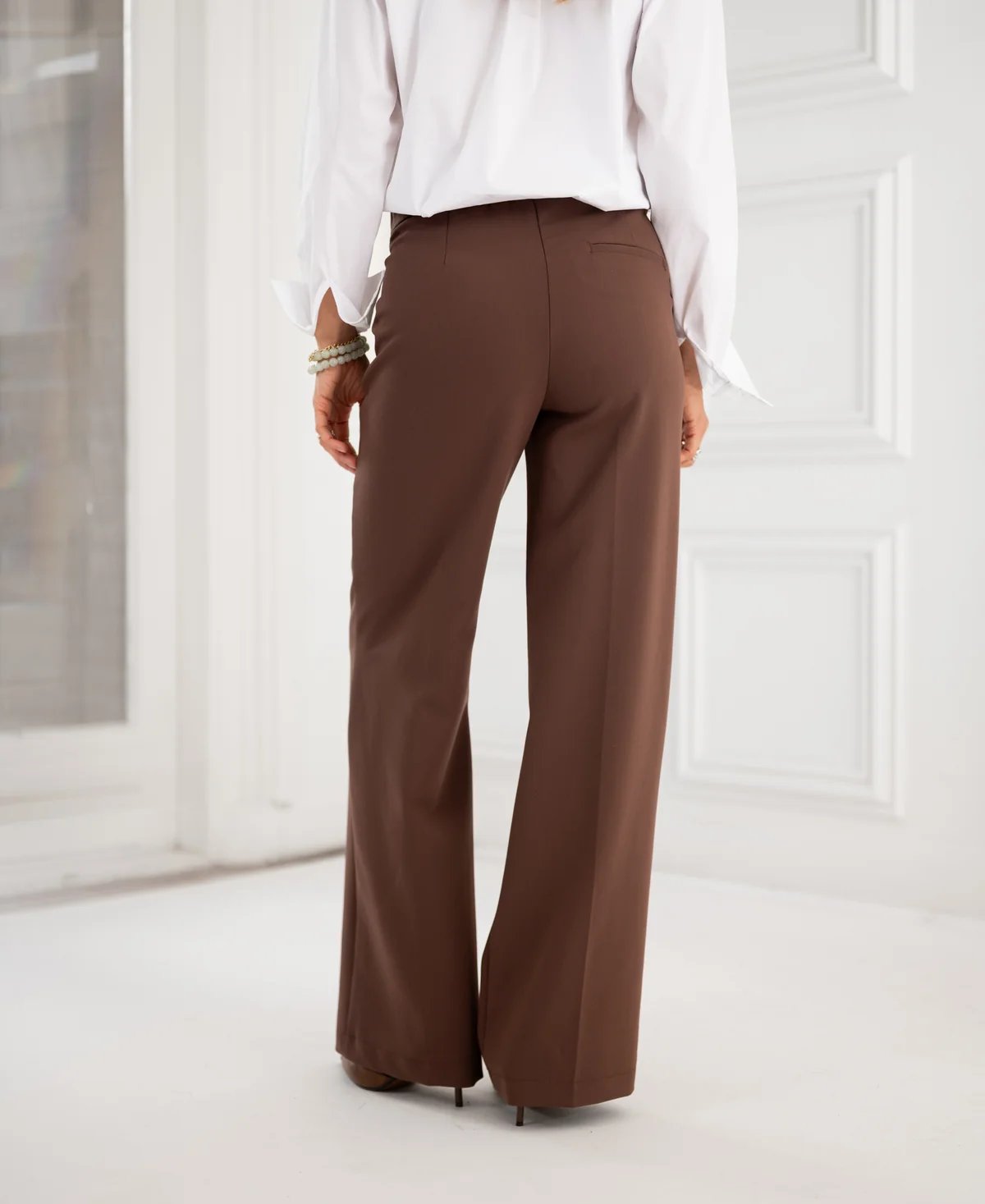 Rear view of a person wearing a white shirt and brown wide-leg pants.