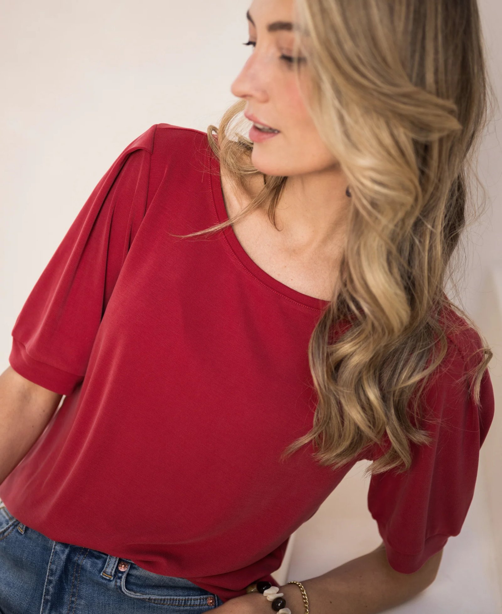 A woman wearing a red puff-sleeved top and jeans.