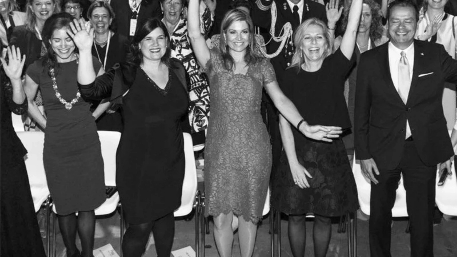 Black and white photo of Queen Máxima and a group of smiling people waving.