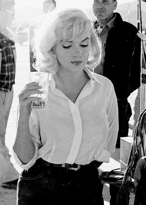 Schwarz-Weiß-Foto von Marilyn Monroe, die ein Glas in der Hand hält und nachdenklich nach unten blickt.