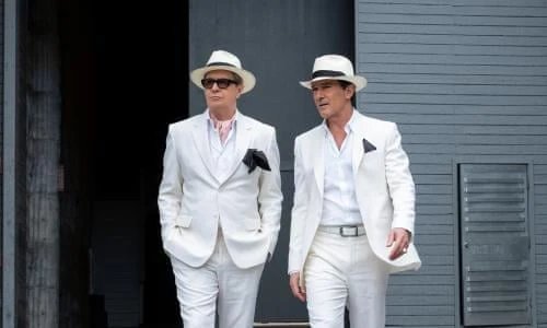 Zwei Männer in weißen Anzügen und mit Fedora-Hüten gehen nebeneinander her.
