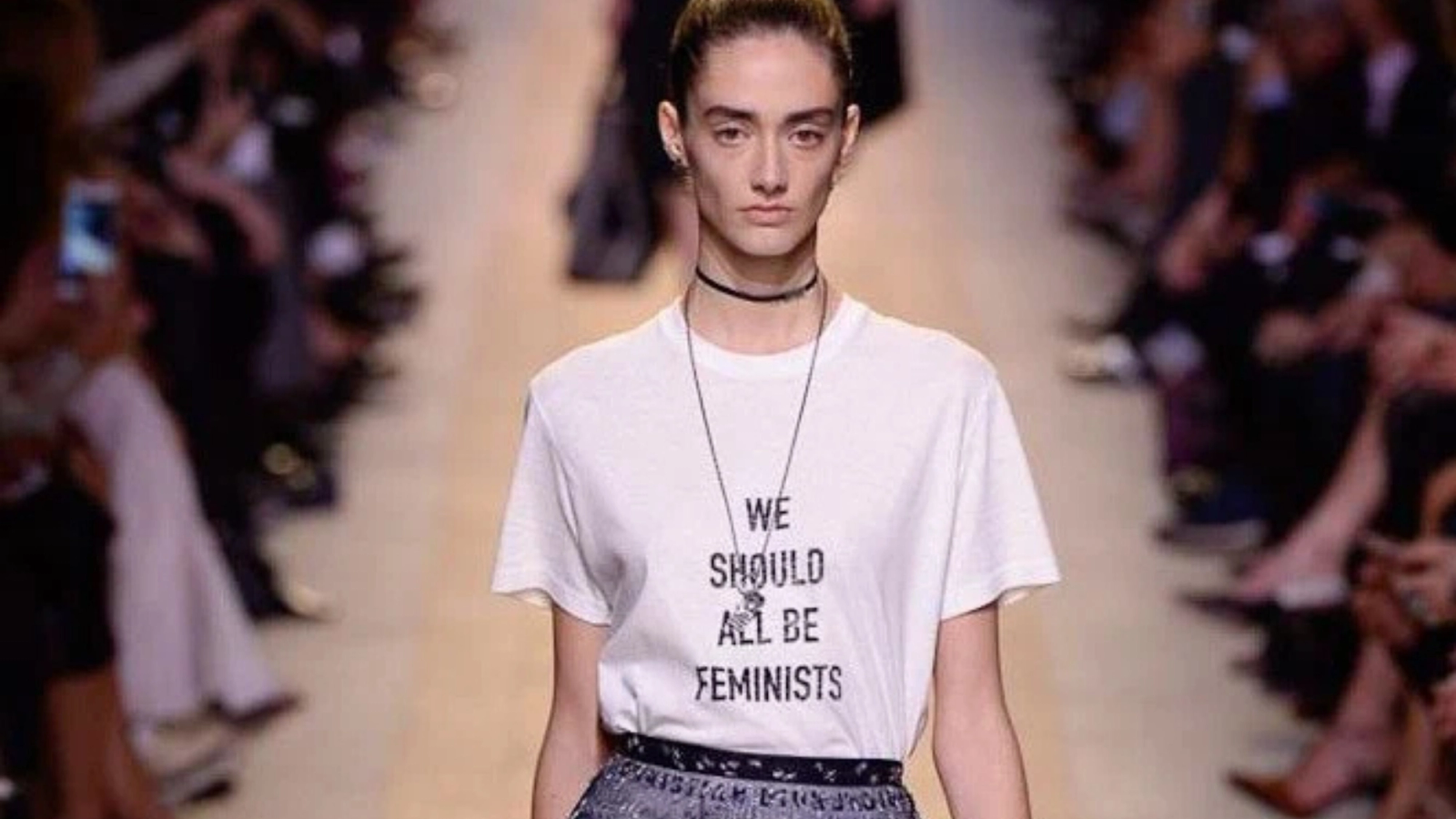 A model on a runway wearing a white T-shirt that reads 