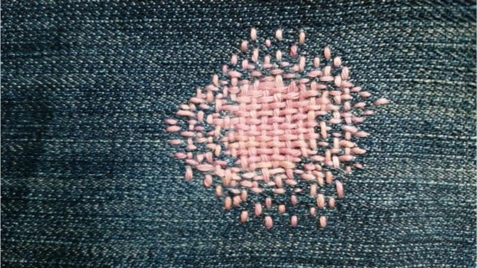 A patch of pink darning stitches on blue denim.