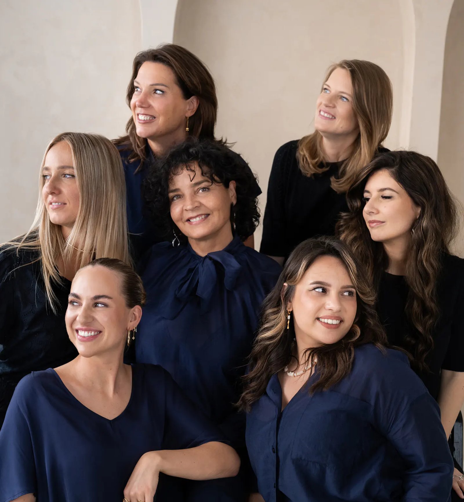 Sieben lächelnde Frauen posieren gemeinsam.