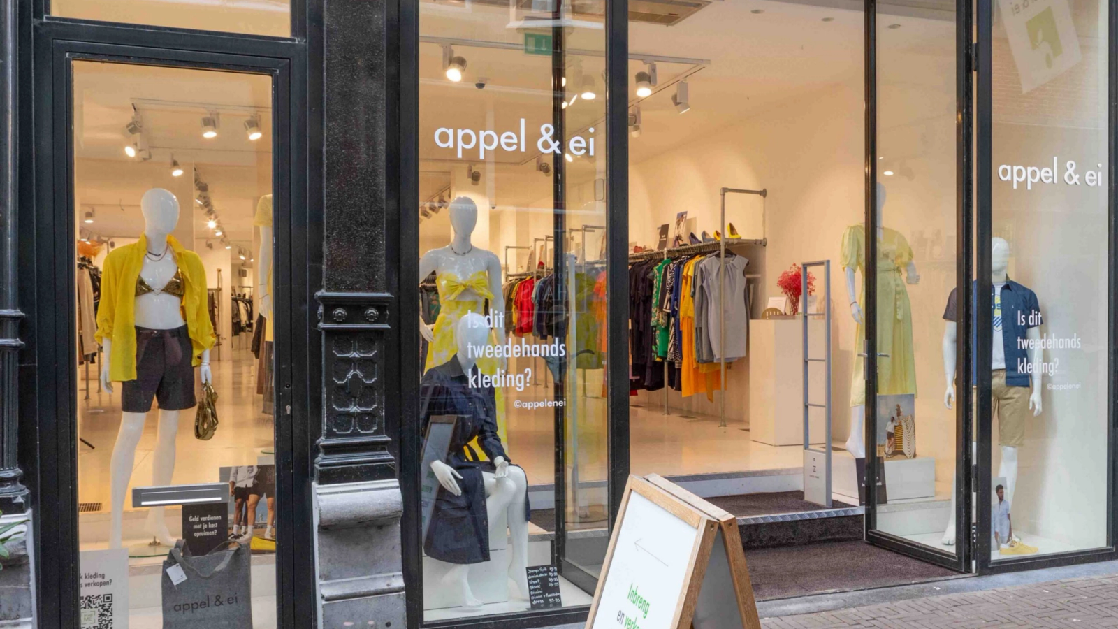 Storefront of 'appel & ei' second-hand clothing store, with mannequins displaying colorful outfits in the windows.