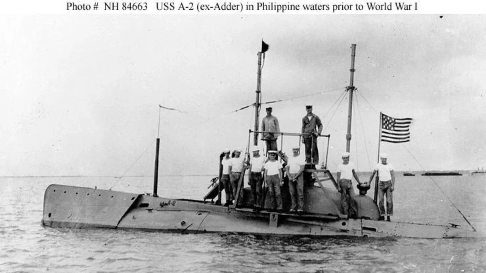 The USS A-2 (formerly the Adder) submarine, with its crew on deck and the American flag flying, in Philippine waters prior to World War I.