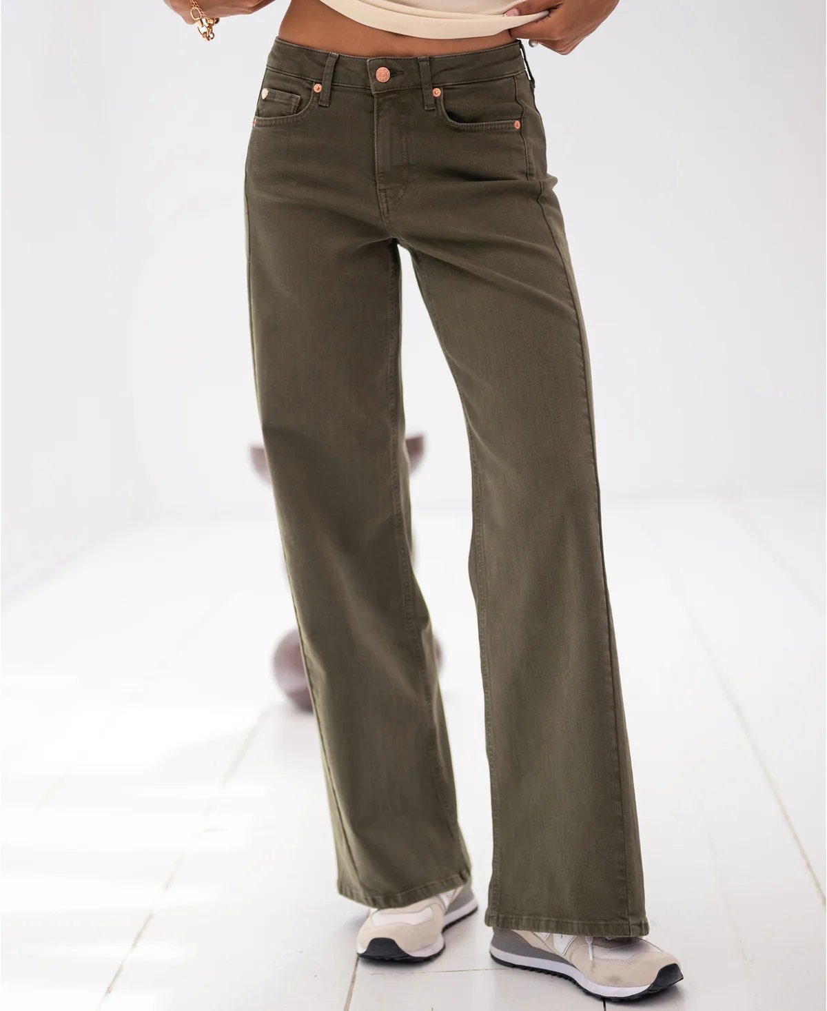 A person wears olive green wide-leg jeans with light sneakers.