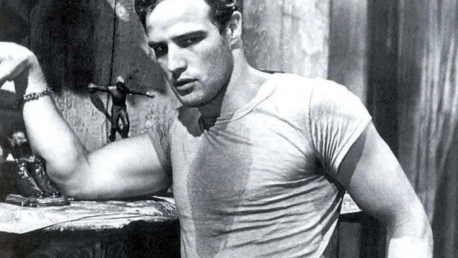 A black-and-white photo of Marlon Brando in a wet, tight T-shirt, looking directly at the viewer.