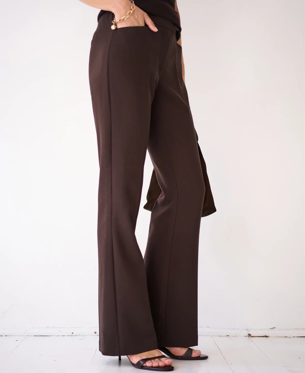 A person's lower body in dark brown cut-out pants and black high-heeled sandals.