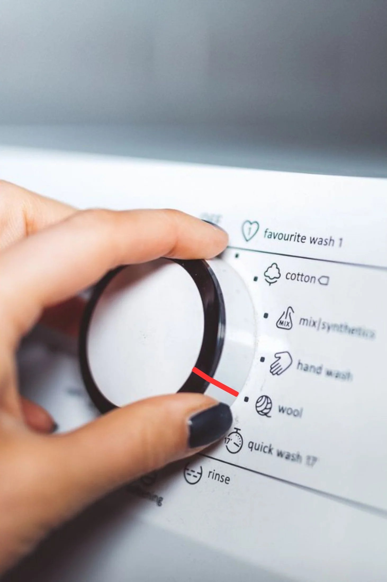 A hand turns the dial on a washing machine that displays various wash cycles.