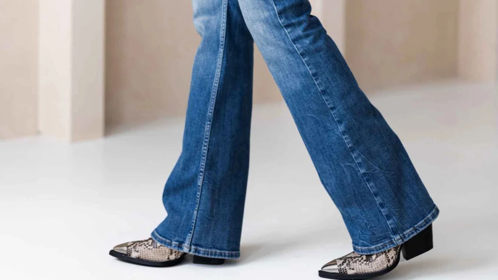 Beine in blauen Flare-Jeans und Cowboystiefeln mit Schlangenmuster beim Gehen.