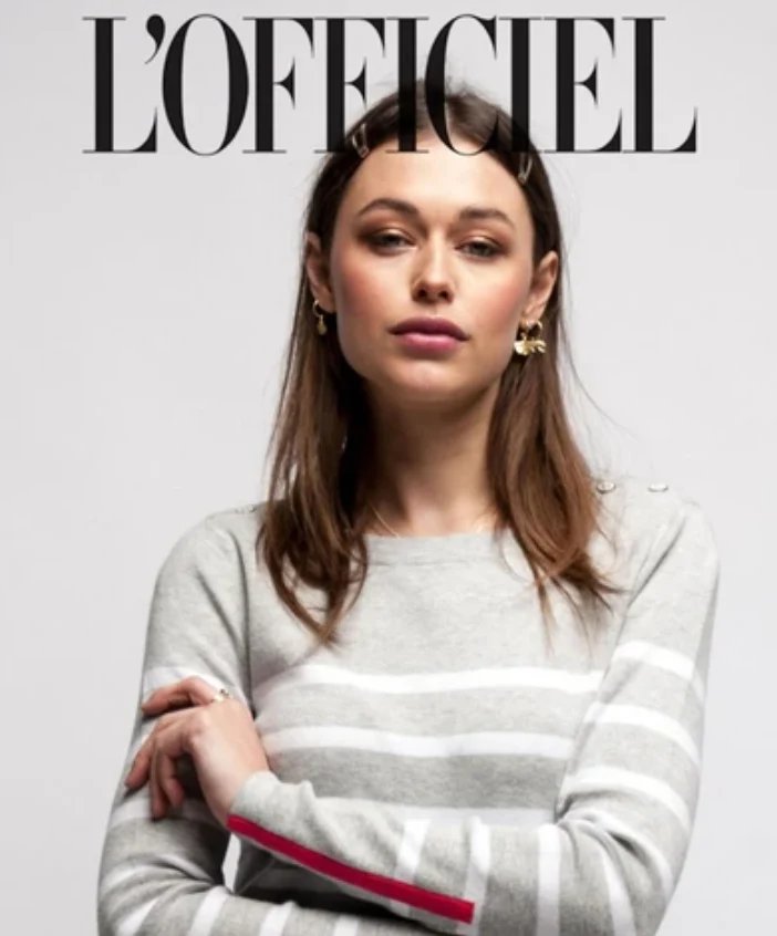The cover of L'OFFICIEL magazine features a model wearing hair clips and a gray-and-white-striped sweater, looking at the camera.