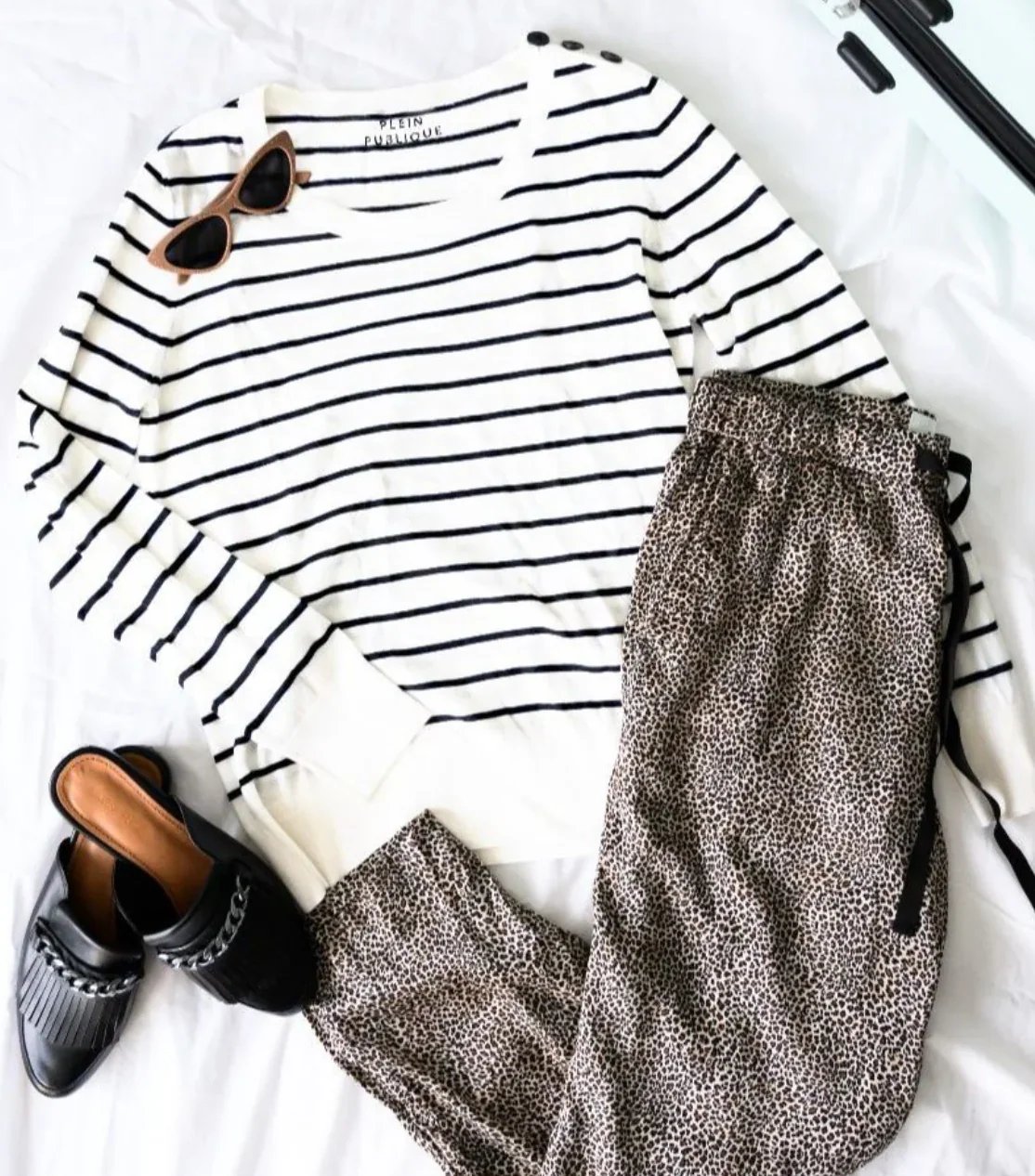 Flat lay of a black and white striped shirt, leopard print pants, black mules, and brown sunglasses.