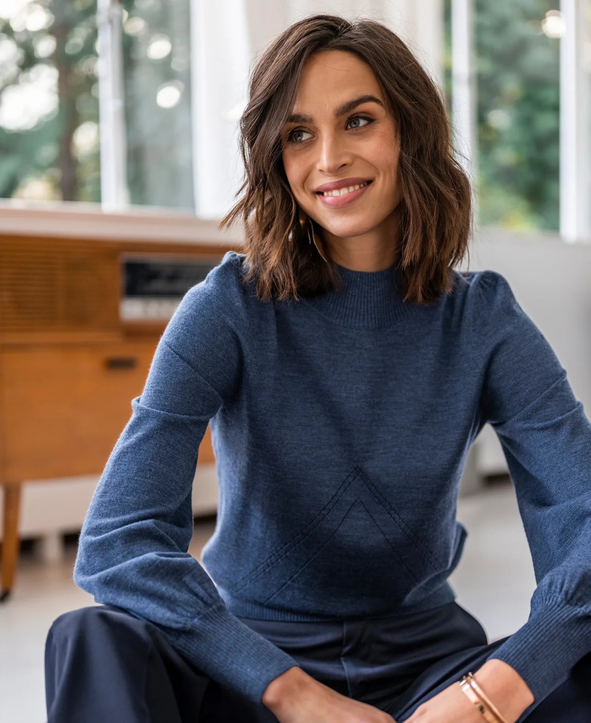 Lächelnde Frau in einem blauen Pullover mit Chevron-Muster, die auf dem Boden sitzt.