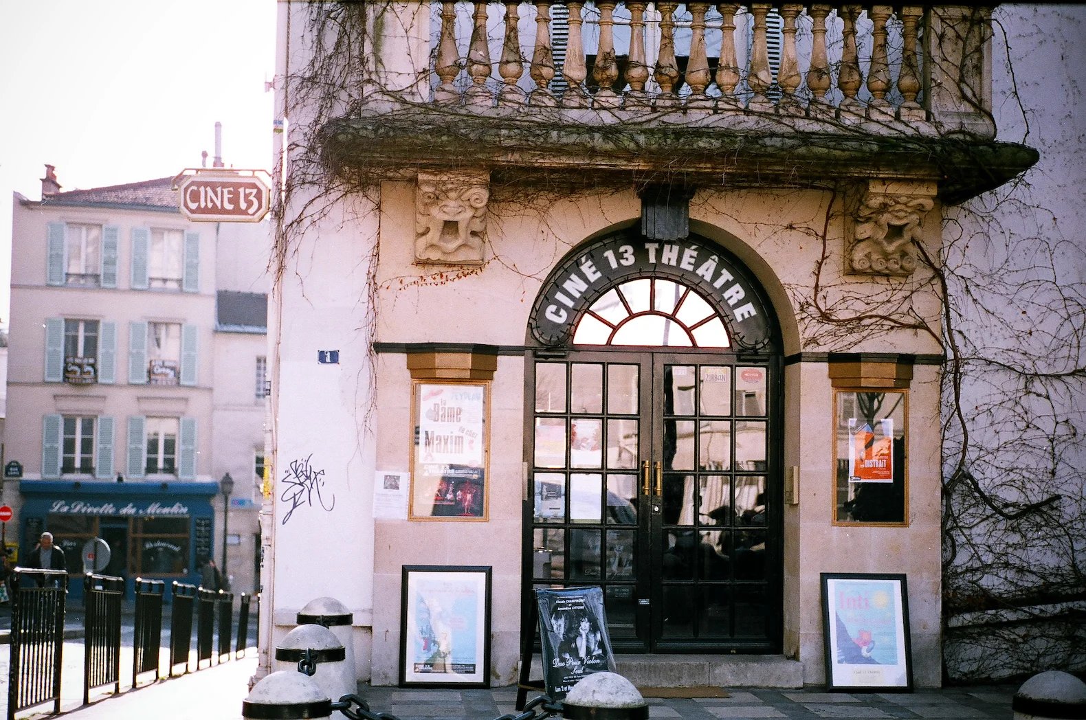 The entrance to Ciné 13 Théâtre, an old building with an arched glass door, bare vines, and movie posters.