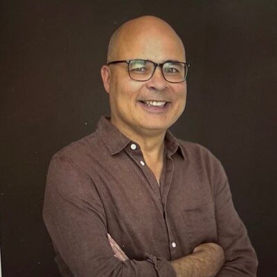 Smiling man with glasses and a brown shirt, arms crossed.