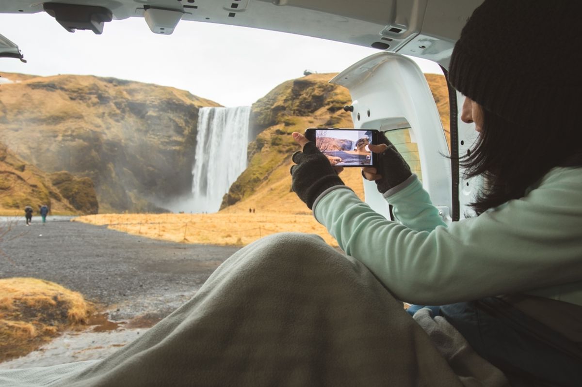 Female tourist is taking photo with mobile phone camera while travel in Iceland stay in campervan by Skogafoss