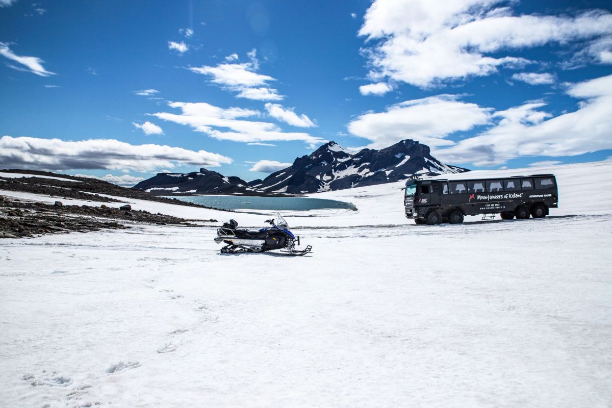 A snowmobile parked on the glacier with mountains and a lake in the distance