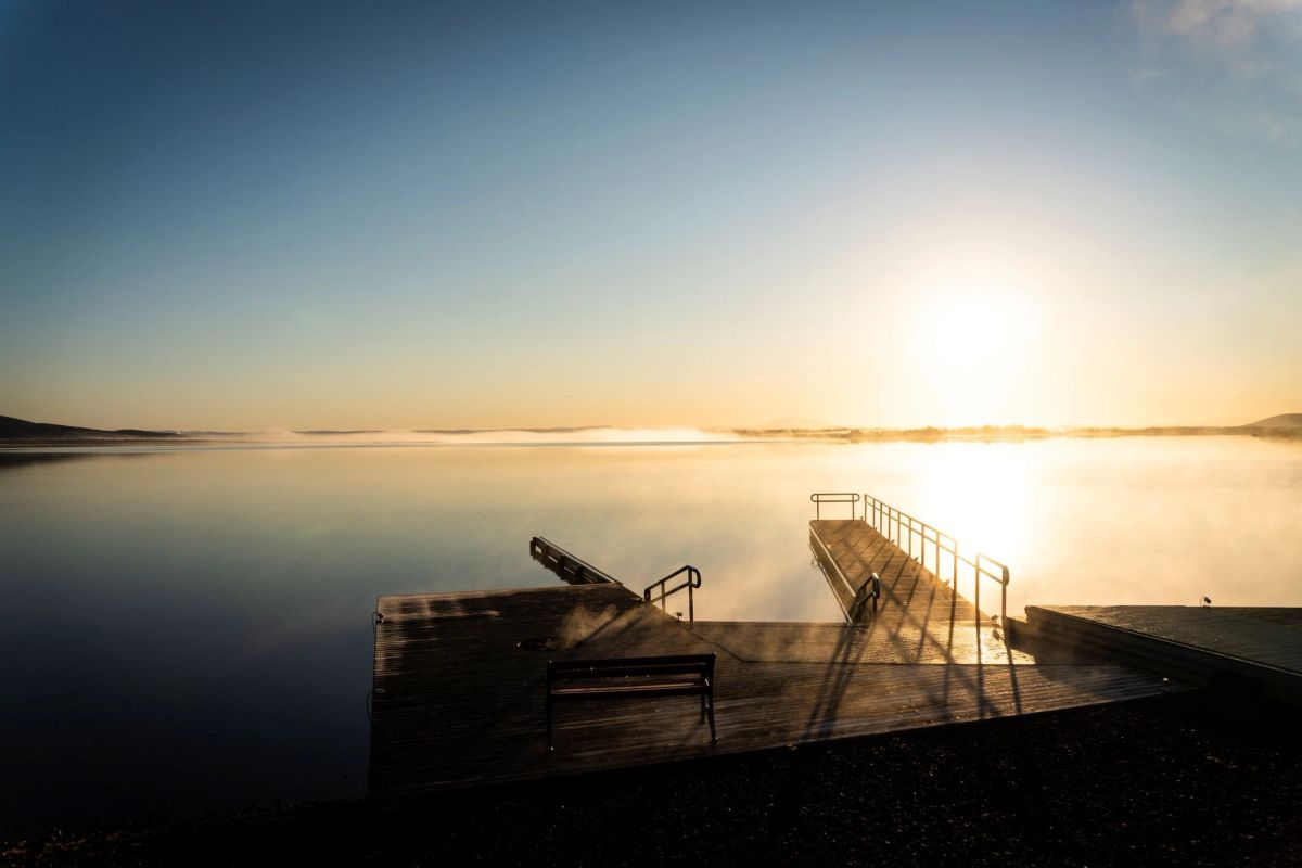 A wooden jetty silhouetted against a low sun rising over a calm lake