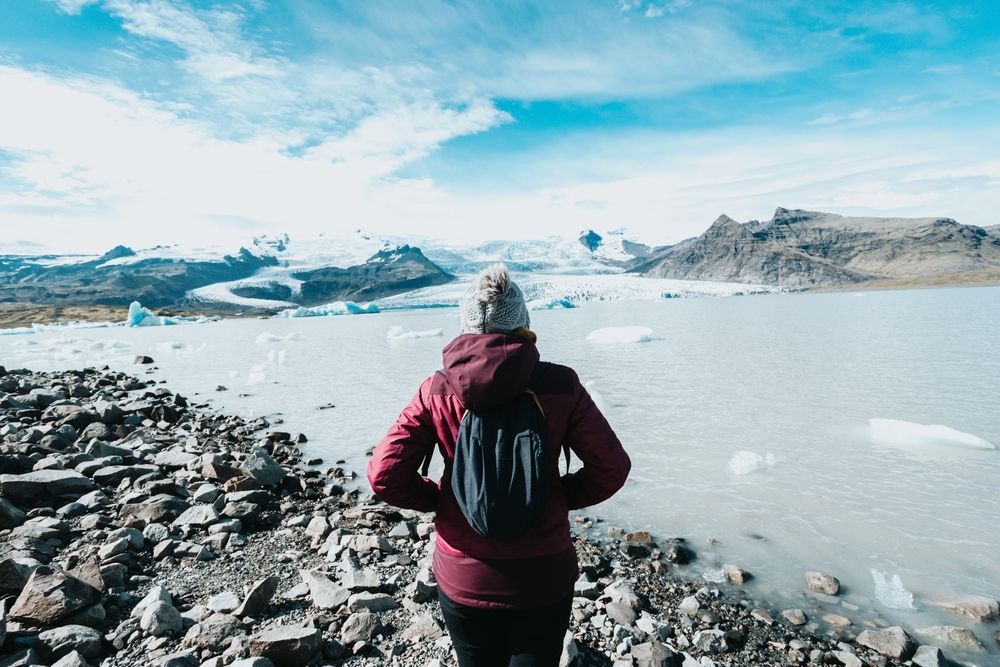 A woman in a red jacket standing at a glacier lagoon