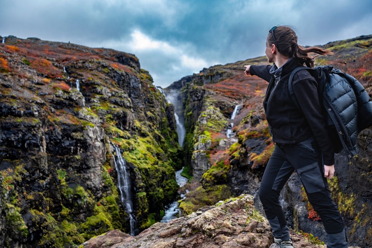 youn woman pointing on glymur waterfall canyon on the cliffs in iceland