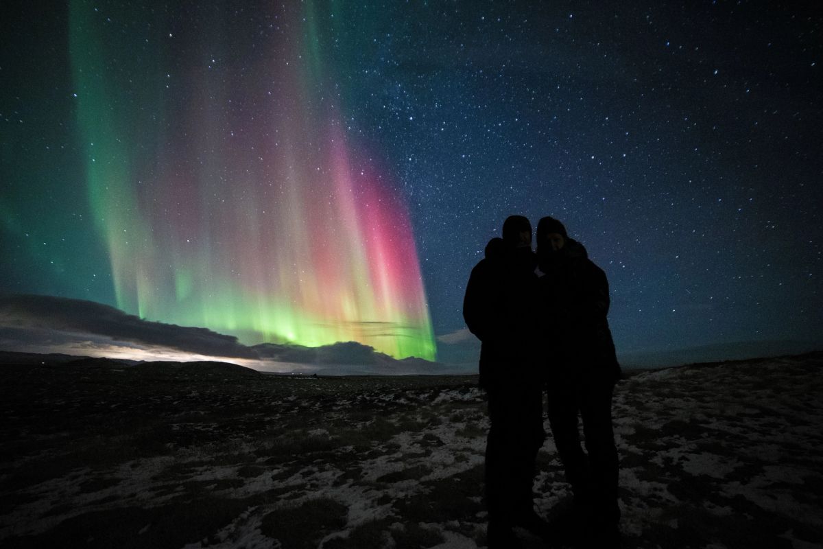 A couple silhouetted against a pink and green aurora