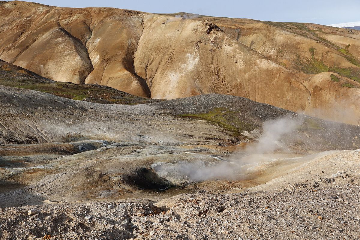 Steam pouring from a vent at the foot of an orange clay slope streaked with pale minerals