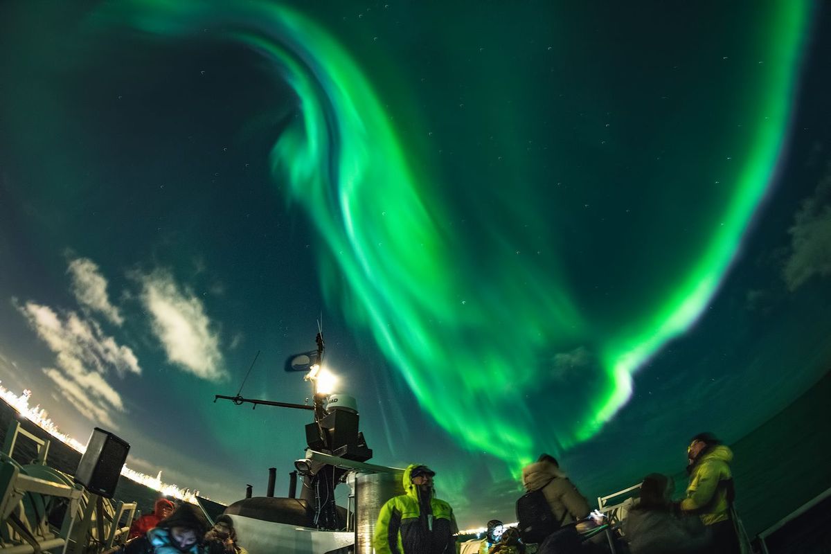 Passengers on a boat watching a green aurora swirl overhead