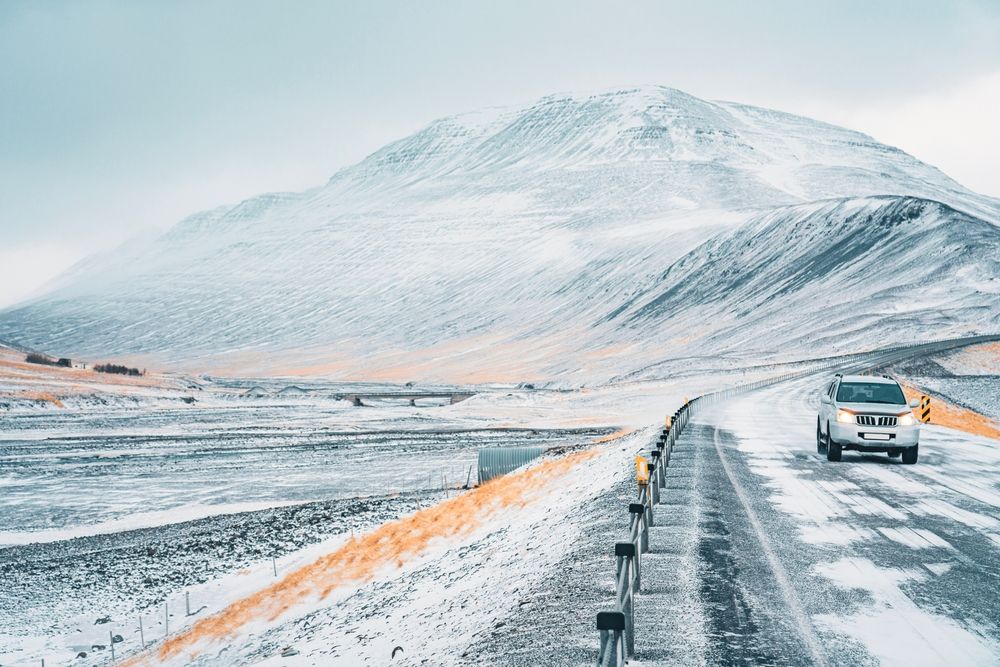 Car driving along an open two-lane road through Iceland's mountain landscape
