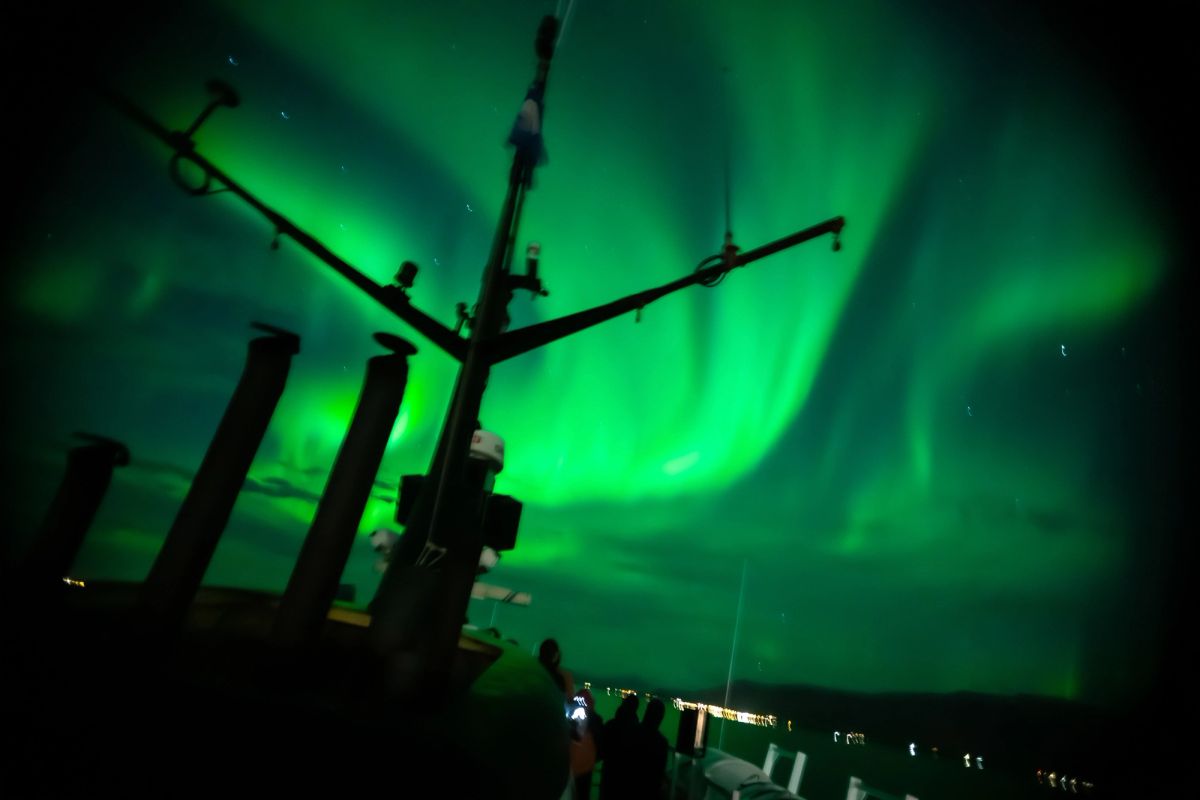 The silhouette of a boat mast against the northern lights