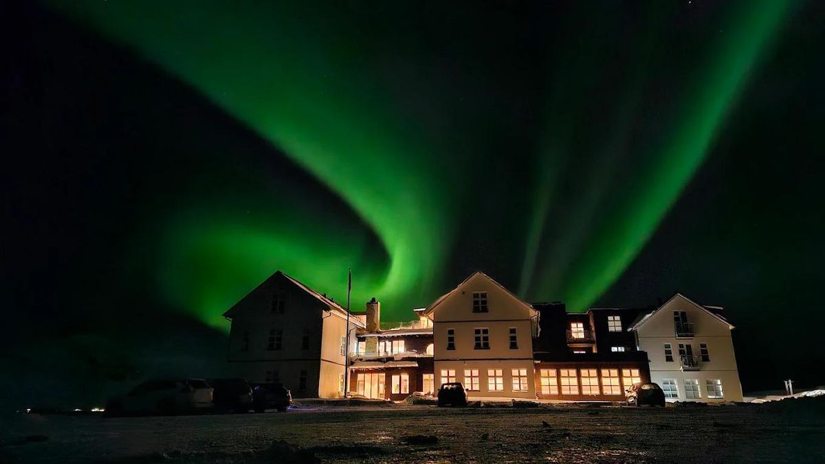 The northern lights above a lit lodge on a snowy hillside