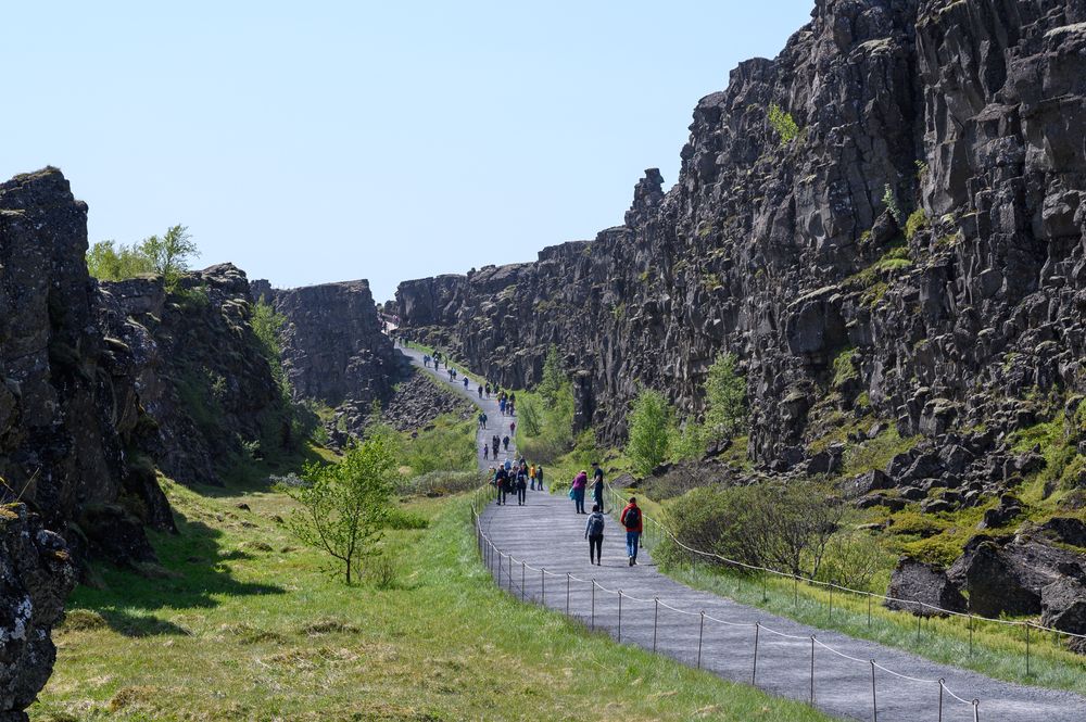 Tourists on walking path among rocks in Thingvellir National park in sunny day