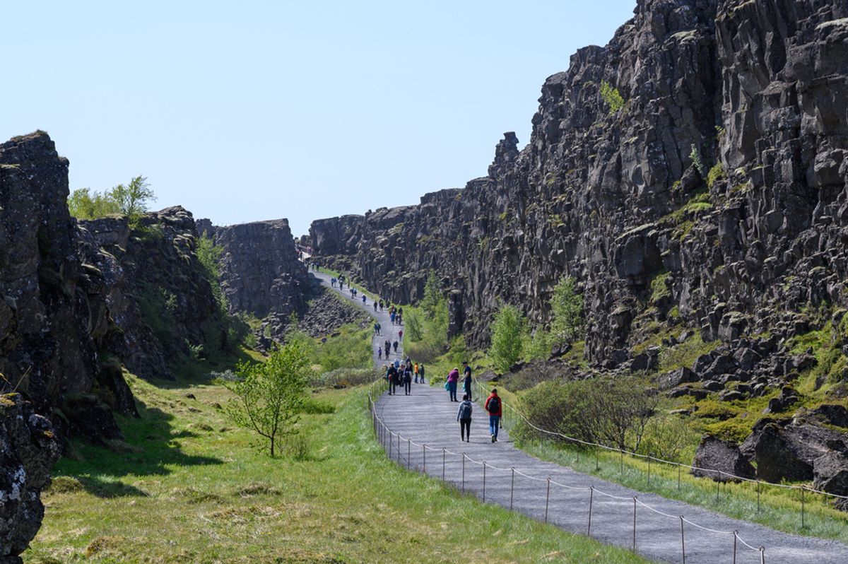 Tourists on walking path among rocks in Thingvellir National park in sunny day
