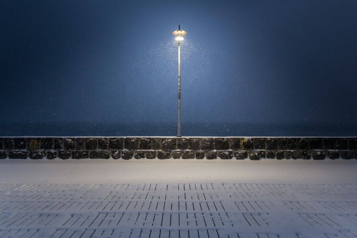 A street light on a snowy Reykjavik waterfront at night, where city light washes out the faint aurora