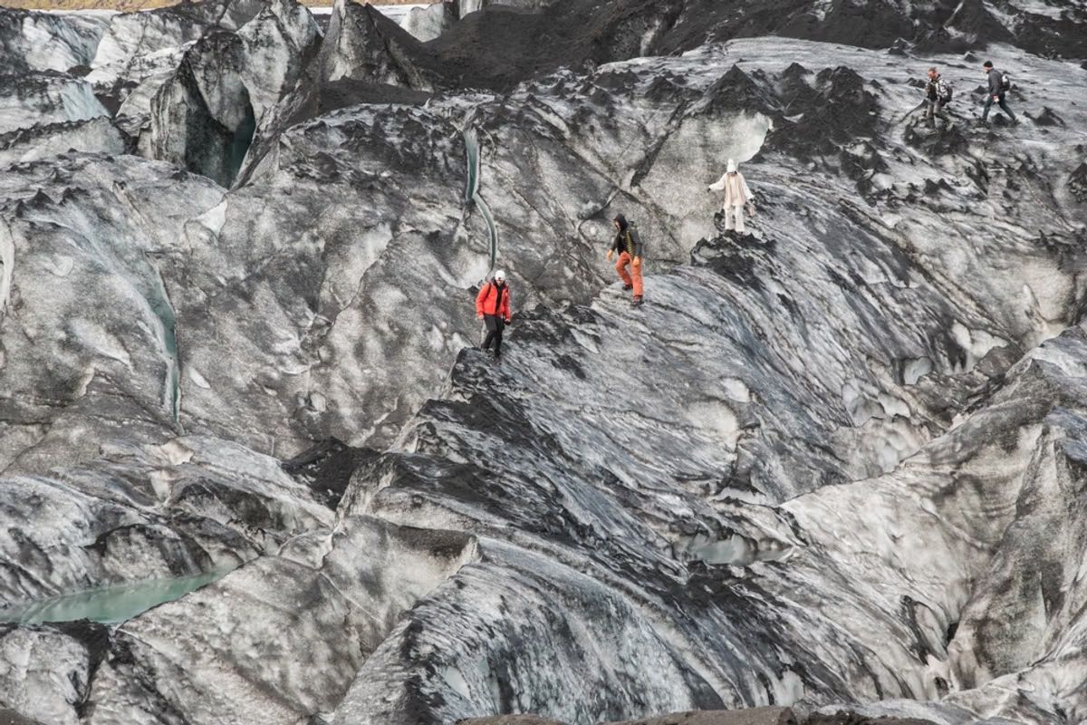 A group of hikers navigating a rugged, icy glacier landscape with steep, crevassed terrain on Solheimajokull glacier