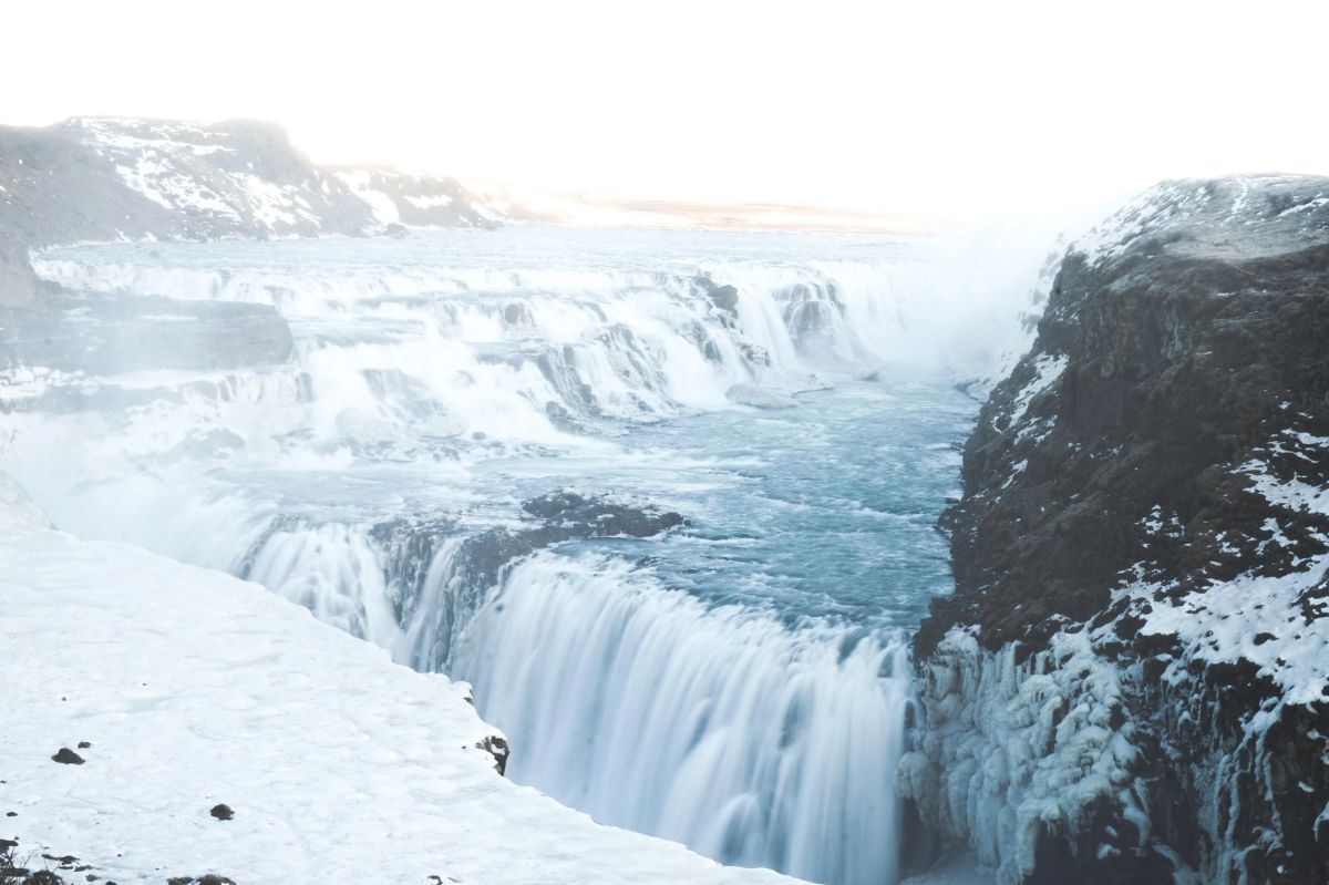 Gullfoss waterfall partly frozen in a snowy canyon under a pale winter sky