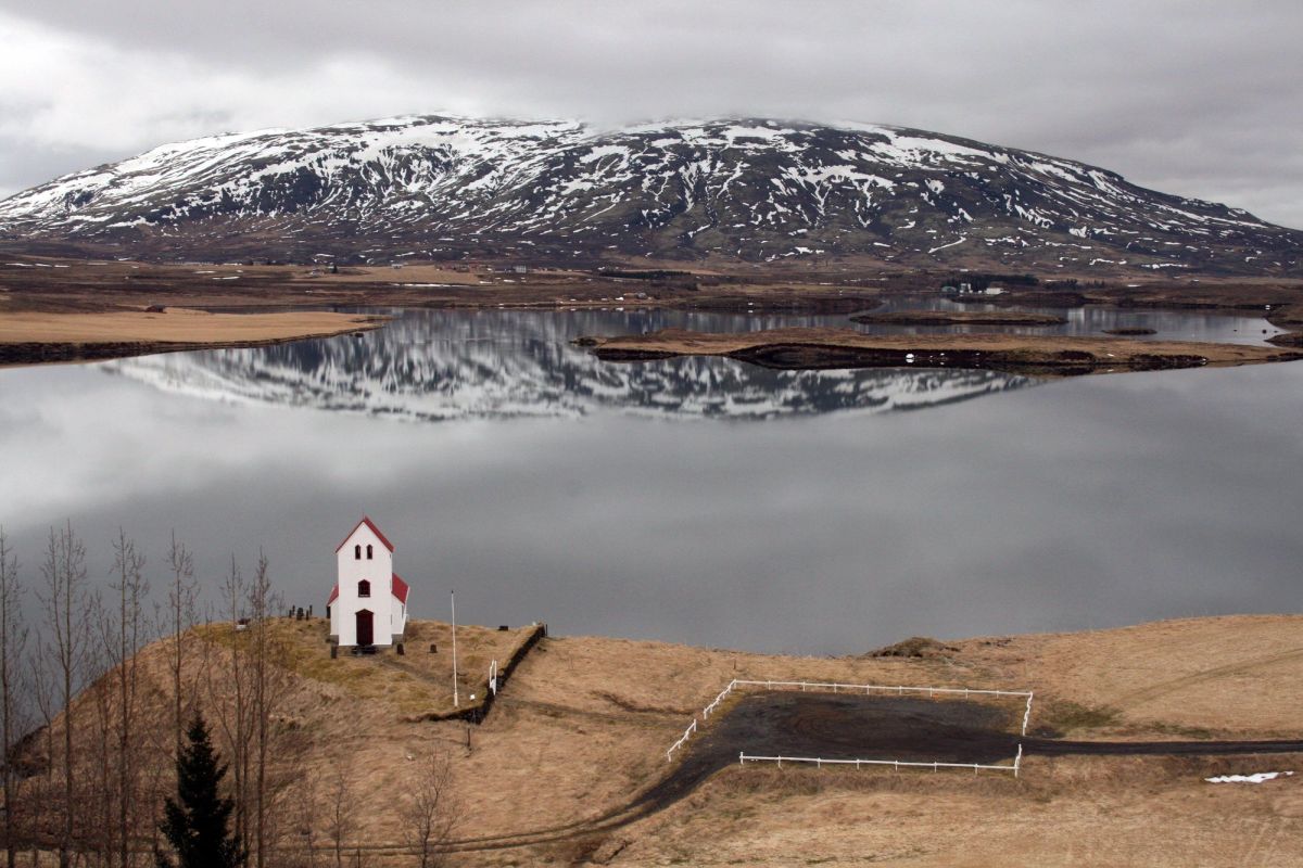 A small church beside a lake with snowy mountains behind