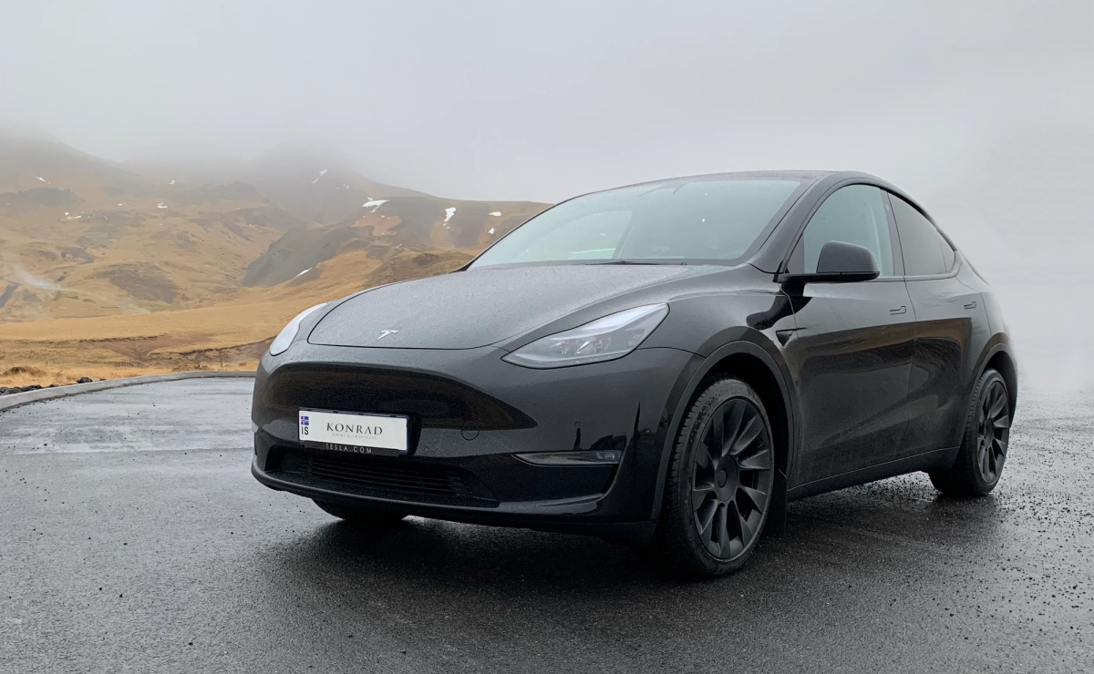 A black Tesla SUV parked on a misty mountain road with mossy hills behind