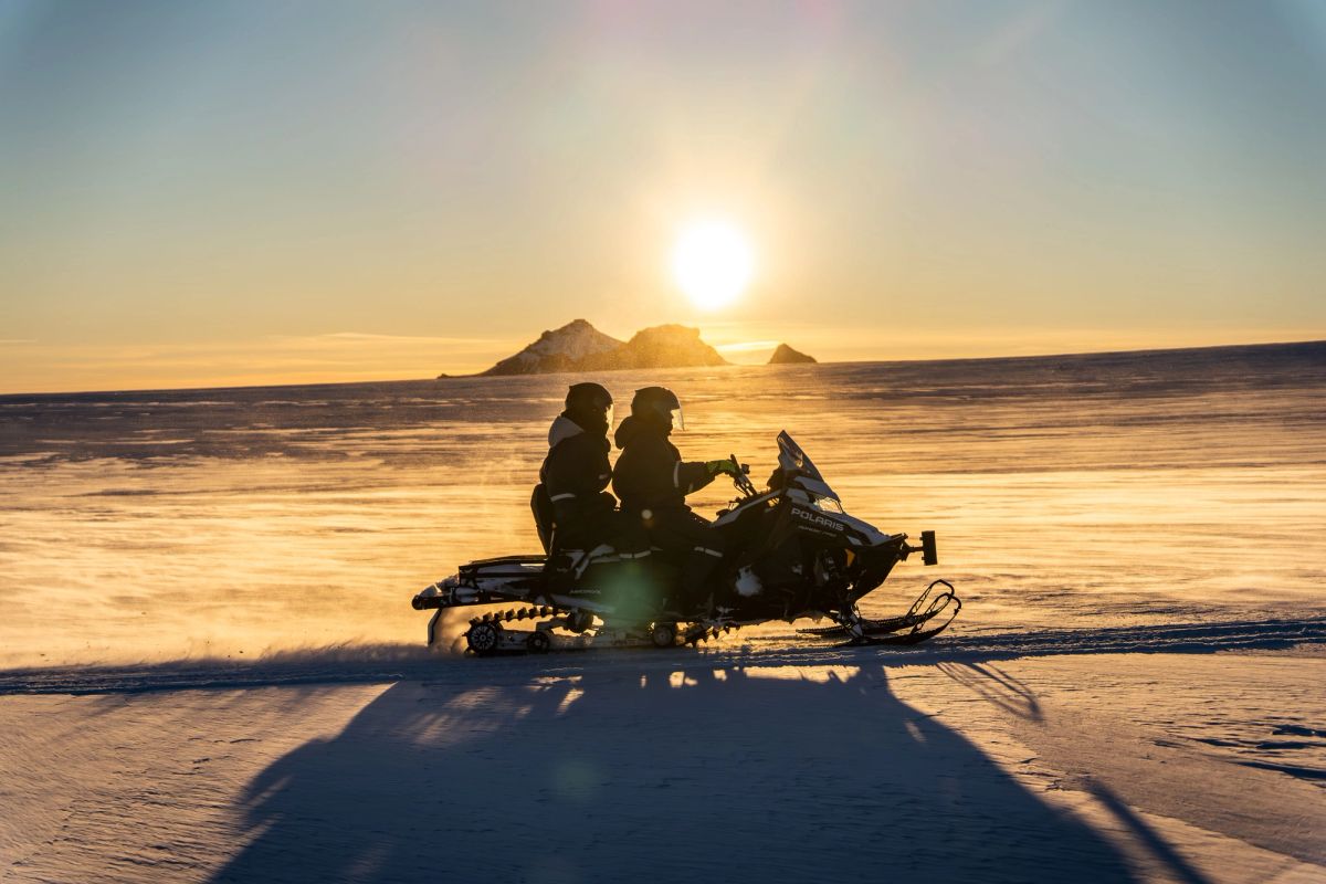 Two people on a snowmobile silhouetted against a low sun on a glacier